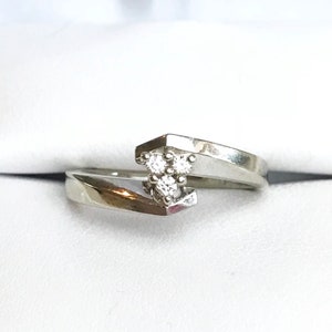 May include: A silver ring with three small diamonds set in a triangular shape. The ring has a unique, twisted design.