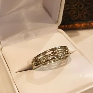May include: A silver ring with a delicate design of small circles and a polished finish. The ring is displayed in a white ring box.