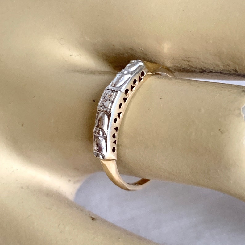 May include: A vintage gold ring with a silver band. The silver band features a repeating pattern of rectangular and curved shapes, with small diamonds set in the center. The ring is on a finger.
