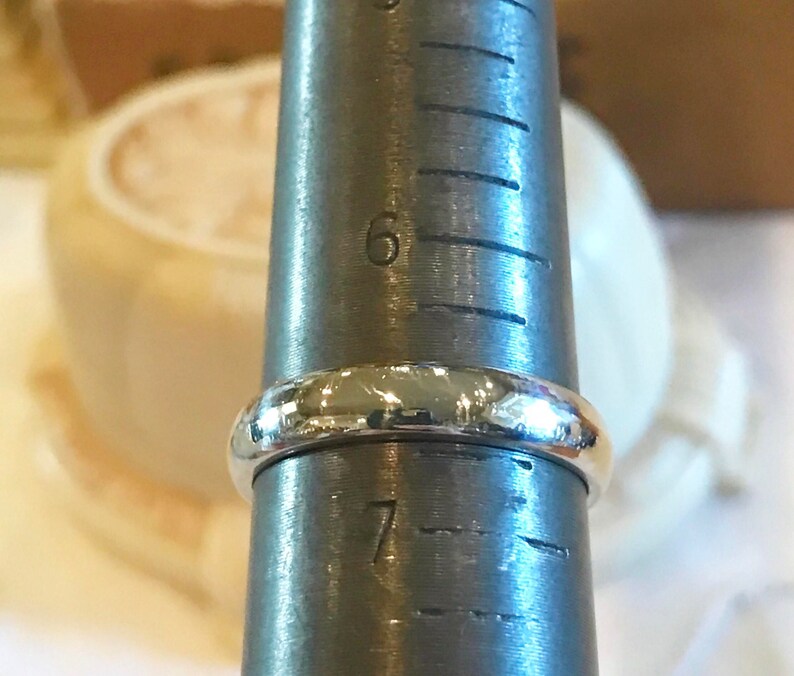 May include: A silver ring being measured on a ring sizer. The ring is a simple band style and is sized between 6 and 7.