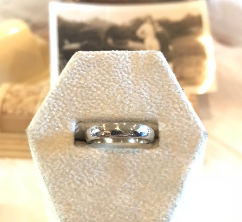 May include: A silver wedding band ring displayed on a white velvet ring box.