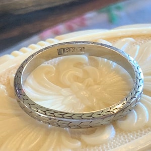 May include: A silver wedding band with a textured design and the inscription "18K" on the inside.