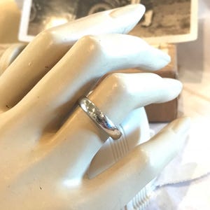 May include: A simple silver wedding band with a smooth, slightly rounded surface.