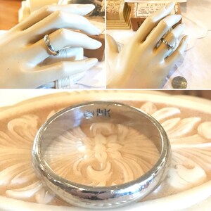 May include: A silver wedding band with a slightly rounded profile and a subtle inscription on the inside of the band. The inscription reads "9 HK".