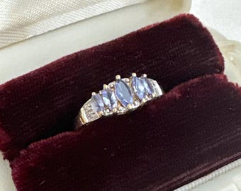 May include: A gold ring with five marquise-shaped purple gemstones and small clear gemstones set in a band.