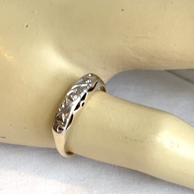 May include: A silver band ring with a delicate, intricate design. The ring is on a mannequin finger.