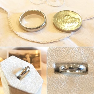 May include: Two silver wedding bands, one in a ring box and one next to a US five-cent coin. The coin is dated 1976 and features the Lincoln Memorial.