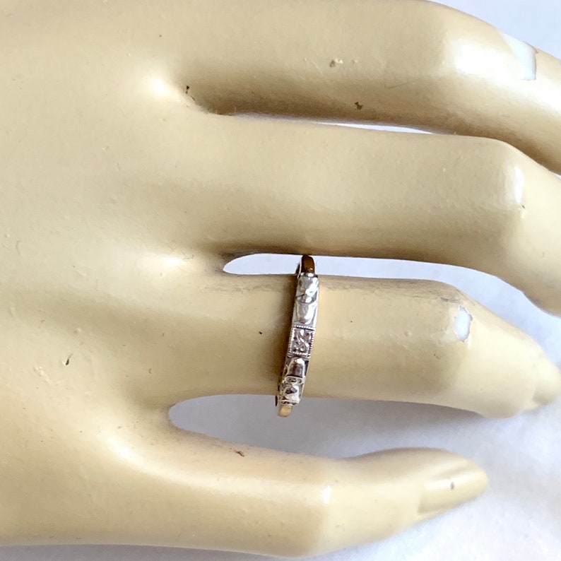 May include: A silver ring with a repeating pattern of small, square designs. The ring is worn on a finger, and the design is visible. The ring appears to be made of metal and has a polished finish. The ring is a piece of jewelry.