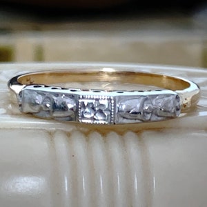 May include: A gold and silver ring with a detailed design. The ring features a band with rectangular silver sections, each with a decorative pattern. The center section has a square design. The ring is likely a piece of jewelry.