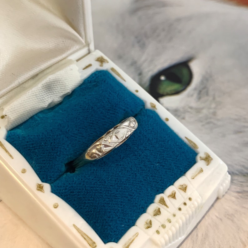 May include: A silver ring with a delicate, intricate design. The ring is displayed in a blue velvet ring box.