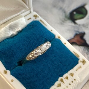 May include: A silver band ring with an intricate engraved design. The ring is displayed in a blue velvet ring box.
