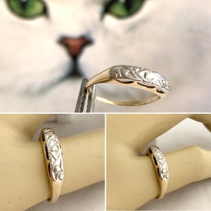 May include: A delicate gold and white two-tone band ring with a floral design. The ring is worn on a model's finger.
