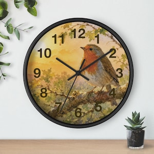 Peut inclure: Une horloge murale ronde avec un cadre noir présentant une illustration à l'aquarelle d'un rouge-gorge perché sur une branche d'arbre sur un fond de lever de soleil doré. Le cadran affiche des chiffres noirs de 1 à 12 et des aiguilles noires.