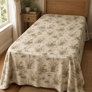 May include: A bedspread featuring a repeating pattern of green frogs, brown cattails, and green lily pads on a cream-colored background. The fabric covers a single bed with a wooden headboard, draping over the sides to display the detailed pond-themed print.