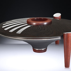 Puede incluir: Una bandeja de servir de madera negra con un borde plateado y líneas blancas. La bandeja tiene un centro redondo y cóncavo y cuatro patas de madera roja.