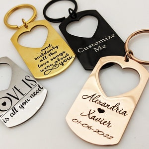 May include: Four heart-shaped keychains with different engravings. One keychain is silver with the text "LOVE IS is all you need". Another keychain is gold with the text "...and suddenly all the love songs were about you". A third keychain is black with the text "Customize Me". The fourth keychain is rose gold with the text "Alexandria Xavier 01-06-2022".