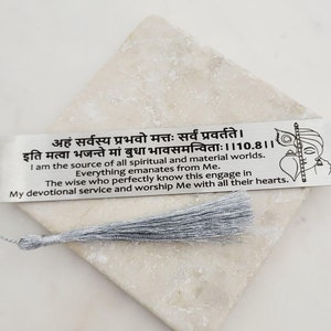 Op de afbeelding: Een zilveren bladwijzer met een kwast. De bladwijzer heeft een Sanskriet citaat en een illustratie van een hindoeïstische godheid. De quote vertaalt zich als "Ik ben de bron van alle spirituele en materiële werelden. Alles komt voort uit mij. De wijzen die dit perfect weten, engageren zich in mijn toegewijde dienst en aanbidden mij met heel hun hart."