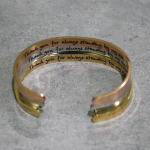 May include: A gold, silver, and rose gold bangle bracelet with the inscription "Thank you for always standing by my side" engraved on each band.
