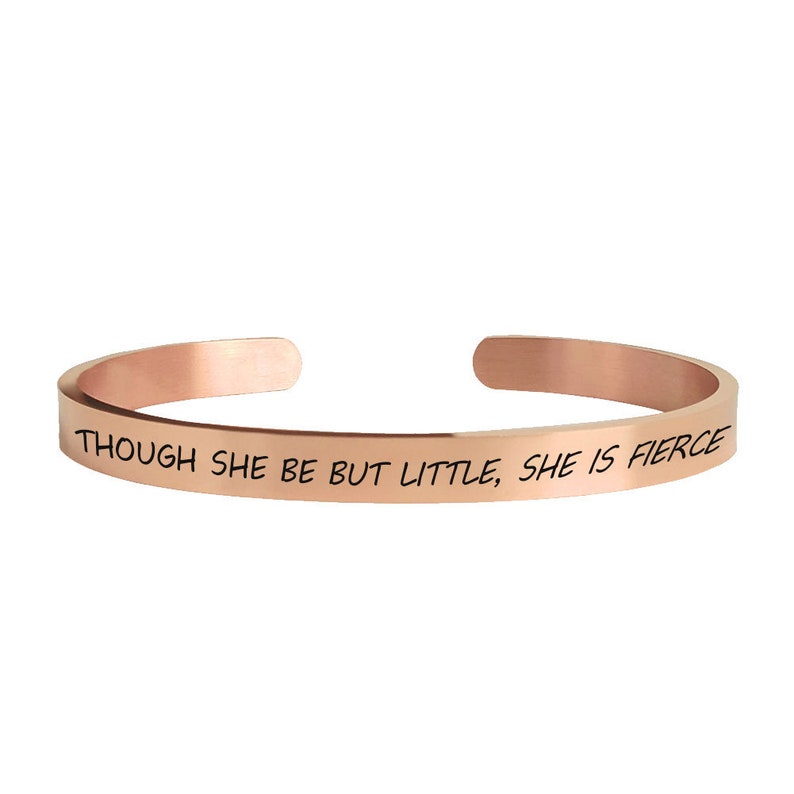 May include: A rose gold bangle bracelet with the inscription "Though she be but little, she is fierce."