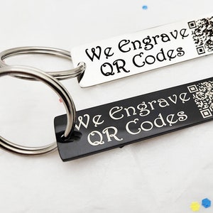 May include: Two silver keychains with black and silver rectangular tags. The tags are engraved with the text "We Engrave QR Codes" and a QR code.