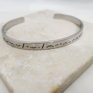 May include: A silver bangle bracelet with a message in braille.
