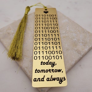 May include: Gold bookmark with a tassel. The bookmark features a heart at the top and the words "today, tomorrow, and always" at the bottom. The bookmark also has a series of binary code printed on it.