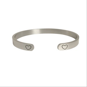 May include: A silver bangle bracelet with two small heart cutouts on the sides.