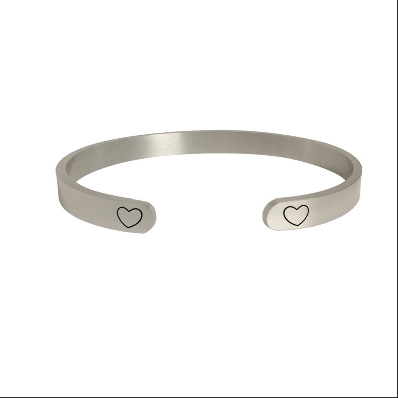 May include: A silver bangle bracelet with two small heart cutouts on the sides.