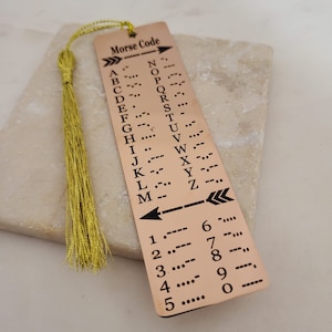 May include: A gold-coloured bookmark with a tassel. The bookmark has a list of the alphabet and numbers in Morse code.