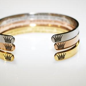 May include: Three stacked bracelets with a crown design on each end. The bracelets are silver, rose gold, and gold.