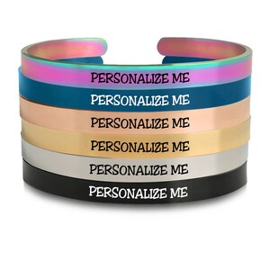 May include: A stack of six metal bracelets in different colors, including iridescent, teal, rose gold, gold, silver, and black. Each bracelet has the text "PERSONALIZE ME" engraved on it.
