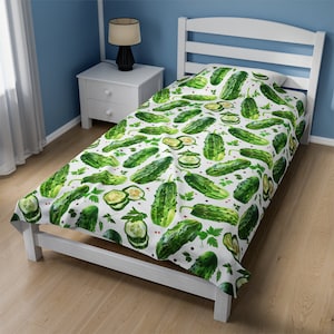 May include: White single bed duvet cover with a repeating pattern of green pickles, pickle slices, and parsley sprigs. Small red peppercorns are scattered across the white background. The duvet cover is on a white bed frame.