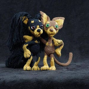 Peut inclure: Deux chiens en peluche crochetés, l'un noir et l'autre brun, debout côte à côte. Le chien noir a de longues oreilles duveteuses et un nez brun. Le chien brun a un museau plus court et des yeux verts.