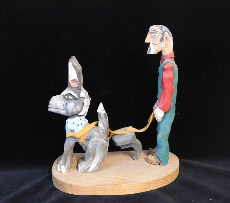 May include: A hand-carved wooden figurine of a man in overalls walking a dog. The man is painted in red, green, and white, and the dog is painted in black, white, and blue.