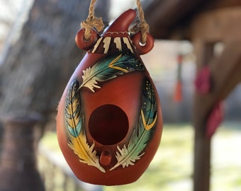 May include: A terracotta birdhouse with a hanging rope, painted with colorful feathers and a small opening for birds to enter.