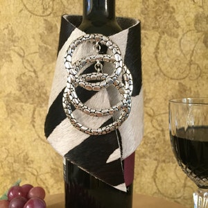 Wine Bottle Wrap/Cover/Cozy Made of Black and White Cowhide with an Antiqued Silver Colored Three Ring Charm.  Great Gift for Wine Lover.