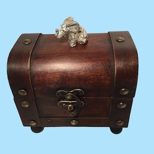 May include: A small wooden treasure chest with a metal elephant figurine on top. The chest has a brown stain finish and metal accents.