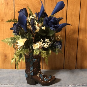 Bota marrón con aspecto de piel repujada y cruz y herradura de imitación turquesa. Arreglo floral de flores azules, marfil y blancas.