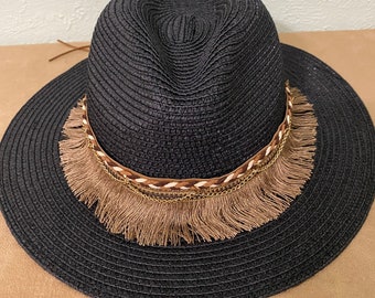 Puede incluir: Un sombrero de paja negro con un ribete trenzado marrón y dorado y una franja marrón.