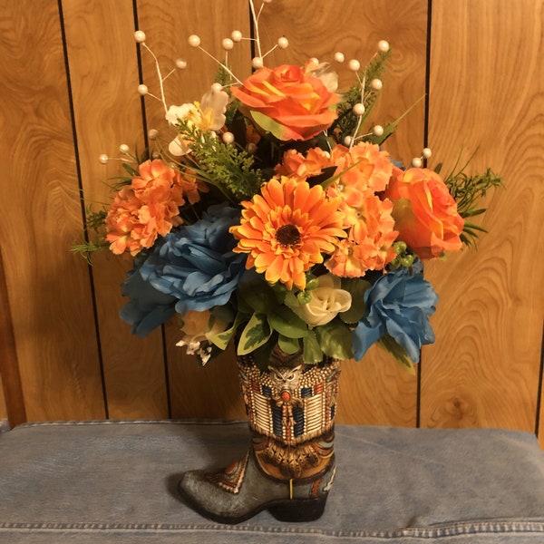 Boot vase with beautiful Indian beading design and ornate owl on side. Flower arrangement of blue, gold and orange flowers with greenery.