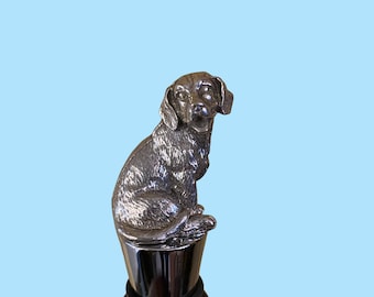 May include: Silver bottle stopper featuring a detailed sculpture of a dog sitting with its head tilted to the side.
