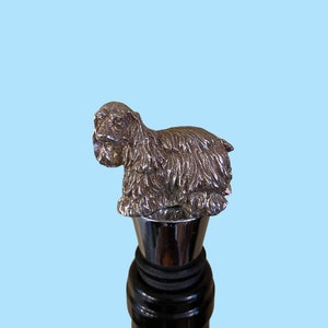 Puede incluir: Tapón de botella plateado con una escultura detallada de un perro Cocker Spaniel. El tapón es de metal y tiene una junta de goma negra.