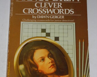 Op de afbeelding: Een bruine boekomslag met de titel "Nancy Drew Clever Crosswords" door Dawn Gerger. De omslag toont een portret van Nancy Drew in een gouden ovale lijst en een kruiswoordpuzzel.