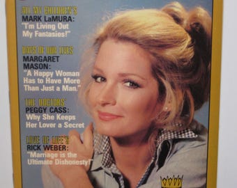 Op de afbeelding: Een tijdschriftcover met een vrouw met blond haar en een blauw-wit geruit overhemd. Het tijdschrift heet "Afternoon TV" en bevat artikelen over de programma's "All My Children", "Days of Our Lives", "The Doctors" en "Love of Life".