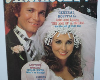 Op de afbeelding: Een tijdschriftcover met een stel in trouwjurken. Het tijdschrift heet "Afternoon TV" en bevat een artikel over de soap "General Hospital" en de personages Luke en Laura. De cover bevat ook informatie over andere soaps, waaronder "Another World", "Guiding Light", "AMC", "OLTL", "DOOL's" en "Y&R's".