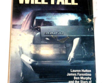 Op de afbeelding: VHS-videocassettehoes voor de film "The Cradle Will Fall". De hoes toont een auto met een hand die uit de kofferbak reikt. De film sterren Lauren Hutton, James Farentino en Ben Murphy.