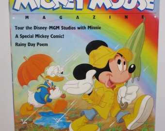 Op de afbeelding: Een vintage Mickey Mouse Magazine cover uit de lente van 1989 met Mickey Mouse en Donald Duck die regenjassen dragen en paraplu's vasthouden. De tekst op de cover luidt "Tour the Disney-MGM Studios with Minnie, A Special Mickey Comic! Rainy Day Poem".