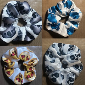 May include: Four different scrunchies with various patterns. The first scrunchie is white with a black koala pattern. The second scrunchie is white with a blue whale pattern. The third scrunchie is white with a black and white panda pattern. The fourth scrunchie is white with a yellow smiley face pattern.