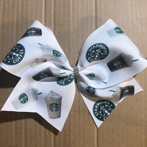 May include: White bow with a Starbucks coffee cup and logo print. The bow is tied with a rhinestone in the center.