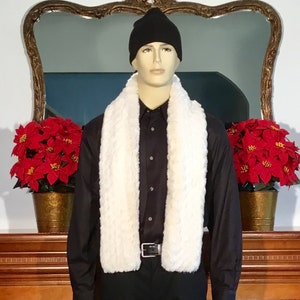 May include: A white faux fur scarf with a black beanie and a black button-down shirt. The scarf is worn around the neck and the beanie is on the head. The person is standing in front of a mirror with red poinsettia plants on either side.